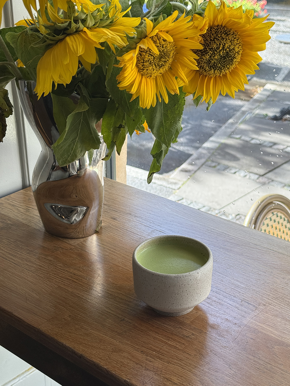 Solsikker i en vase og en kop matcha på et bord ved vinduet