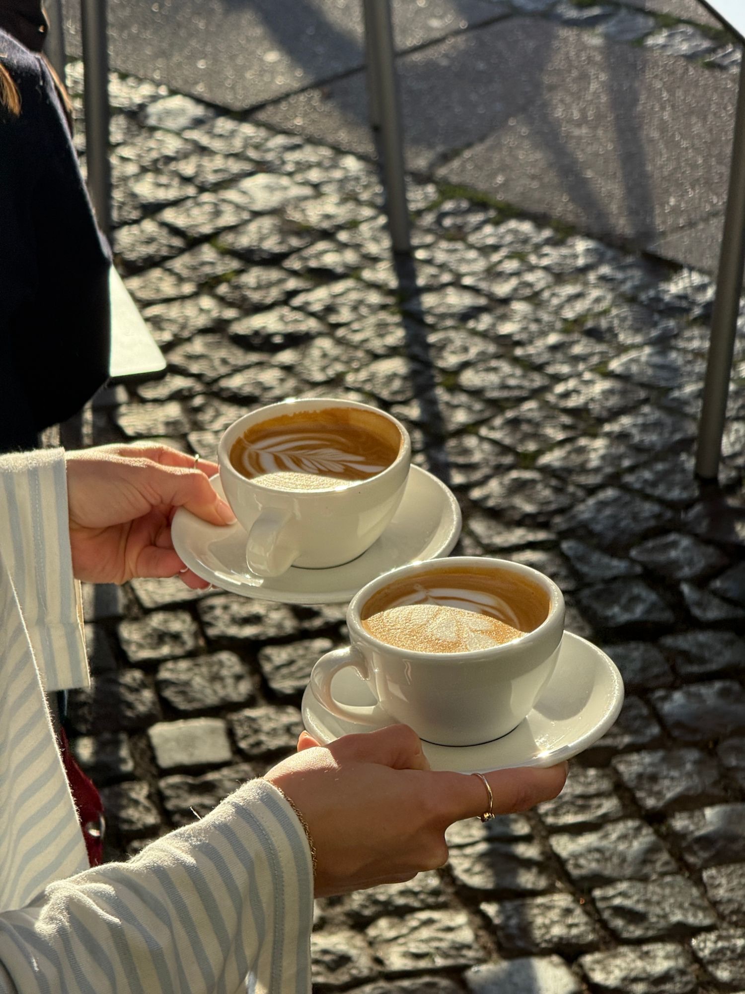 To kopper kaffe med latte art rakt frem i solen over brosten